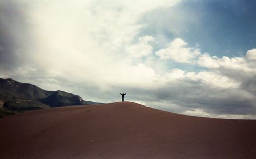 Mid distance view of man standing on mountain against cloudy sky