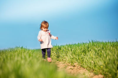 Rear view of boy standing on field against clear sky