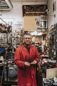 Portrait of smiling mature male locksmith wearing red coat in workshop