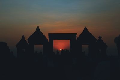 Silhouette people in illuminated building against sky during sunset