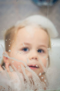 Close-up of toddler covered in soap sud seen through glass