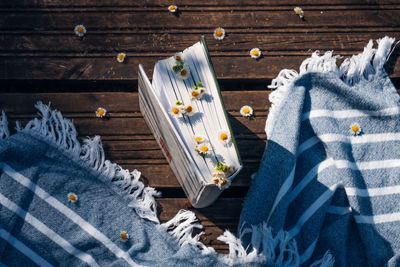 High angle shot of the book on the wooden floor, with blue towel and daisy flowers.