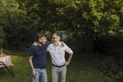 Laughing son and father with arm around standing in back yard