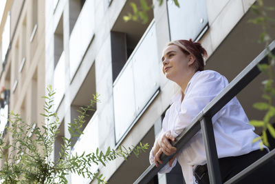 Bottom view against background of high-rise building with trees young business woman 20s looking