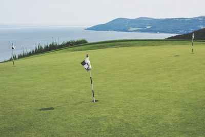 Flags on golf course by sea against sky