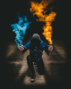 Full length of man wearing hooded shirt while holding distress flare in darkroom