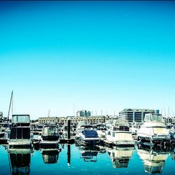 Boats in harbor against clear blue sky