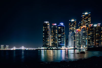 Illuminated city by sea against sky at night