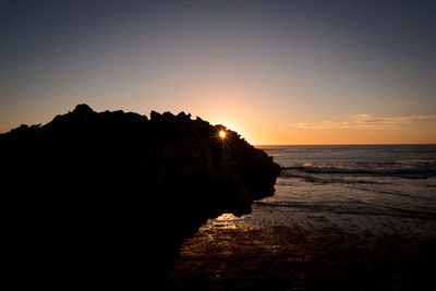 Silhouette rocks on beach against sky during sunset