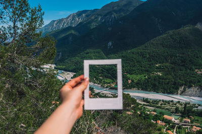 Cropped hand of woman holding picture frame against landscape