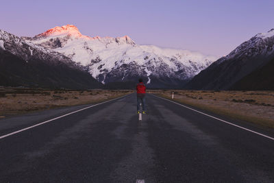 Rear view of man standing on road against sky during winter