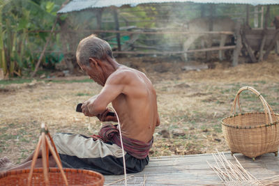 Shirtless senior man making straw basket