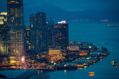 Illuminated modern buildings by sea against sky at night