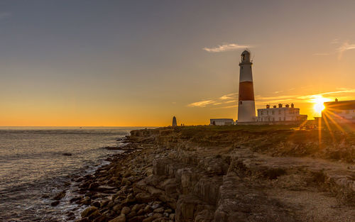 Lighthouse by sea against sky during sunset