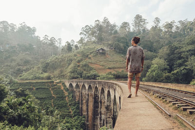 Male tourist walking on fence of bridge in tropical landscape in fog