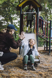 Cheerful girl giving high-five to male teacher while playing on slide at playground