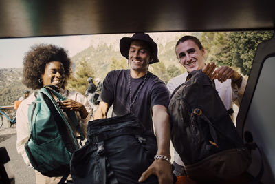 Happy male and female friends unloading luggage from van trunk during road trip