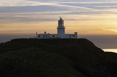 Lighthouse by sea against sky during sunset