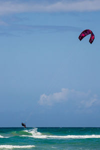 People in sea kite surfing against sky