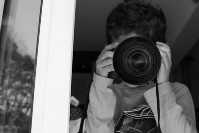 Low angle view of boy photographing with camera seen through window