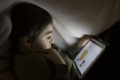 Close-up side view of boy watching movie in digital tablet under blanket at home