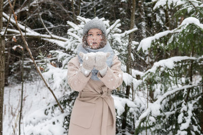 A cute girl in a hat and vazherzh holds snow in her hands and blows on it