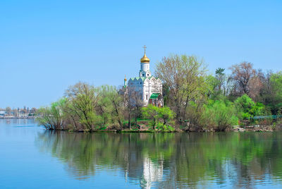 Lighthouse by lake and buildings against clear blue sky