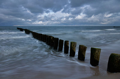 Wooden posts in sea against sky