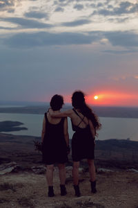 Two woman in black dresses stay on the mountain with a bouquet of flowers in summer at sunset