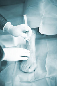 Cropped hands doctor injecting syringe on patient leg in hospital