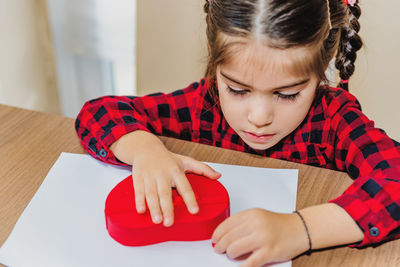 High angle view of girl making heart shape on paper at home