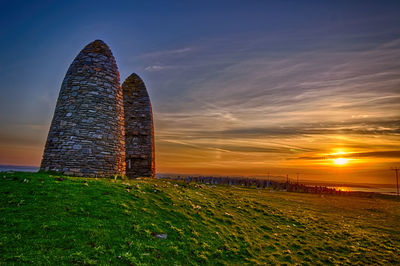 Stone wall on field against sky during sunset