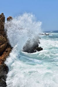 Waves splashing on sea against clear sky