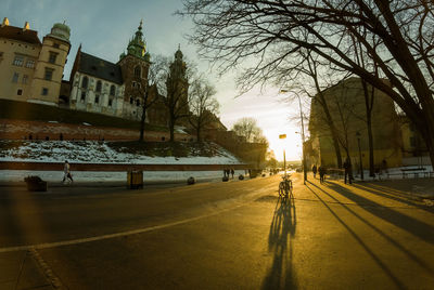 City street by buildings against sky during sunset