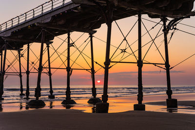 Silhouette bridge over sea against sky during sunset