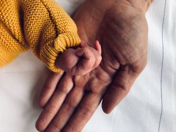 Cropped hands of parent and baby on bed