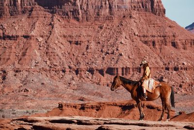 Side view of woman riding horse against rock formation