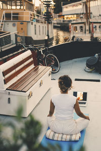 Rear view of woman learning online yoga through laptop in houseboat at harbor