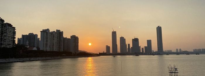 Scenic view of river by buildings against sky during sunset