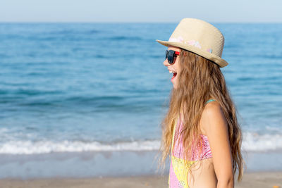 Side view of a girl with an open mouth against the background of the sea and sand.