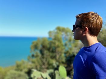 Young man wearing sunglasses against sea and blue sky