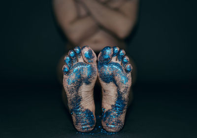 Low section of woman barefoot covered in glitter over black background