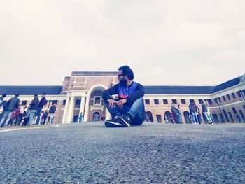 Man sitting on wall in city against sky