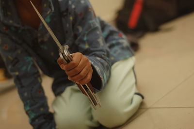 Close-up of boy holding knife while kneeling on floor