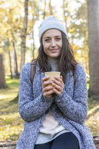 Young woman drinking coffee in park during winter