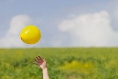 Cropped hand below balloon on field against sky