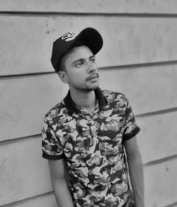 Young man looking away while standing against wall