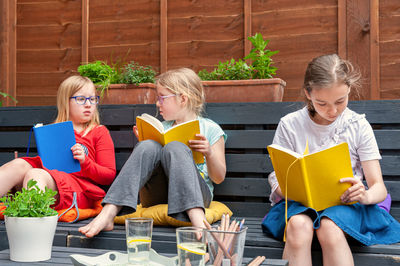 Three school age girls sitting together in garden and doing homework.