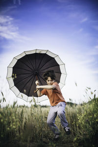 Boy holding umbrella while running on grassy field