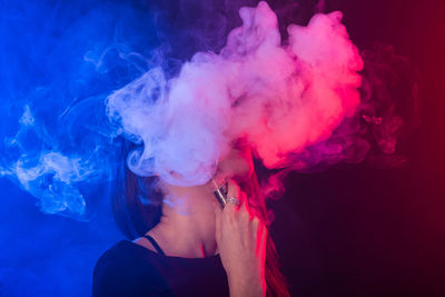 Portrait of woman smoking against black background